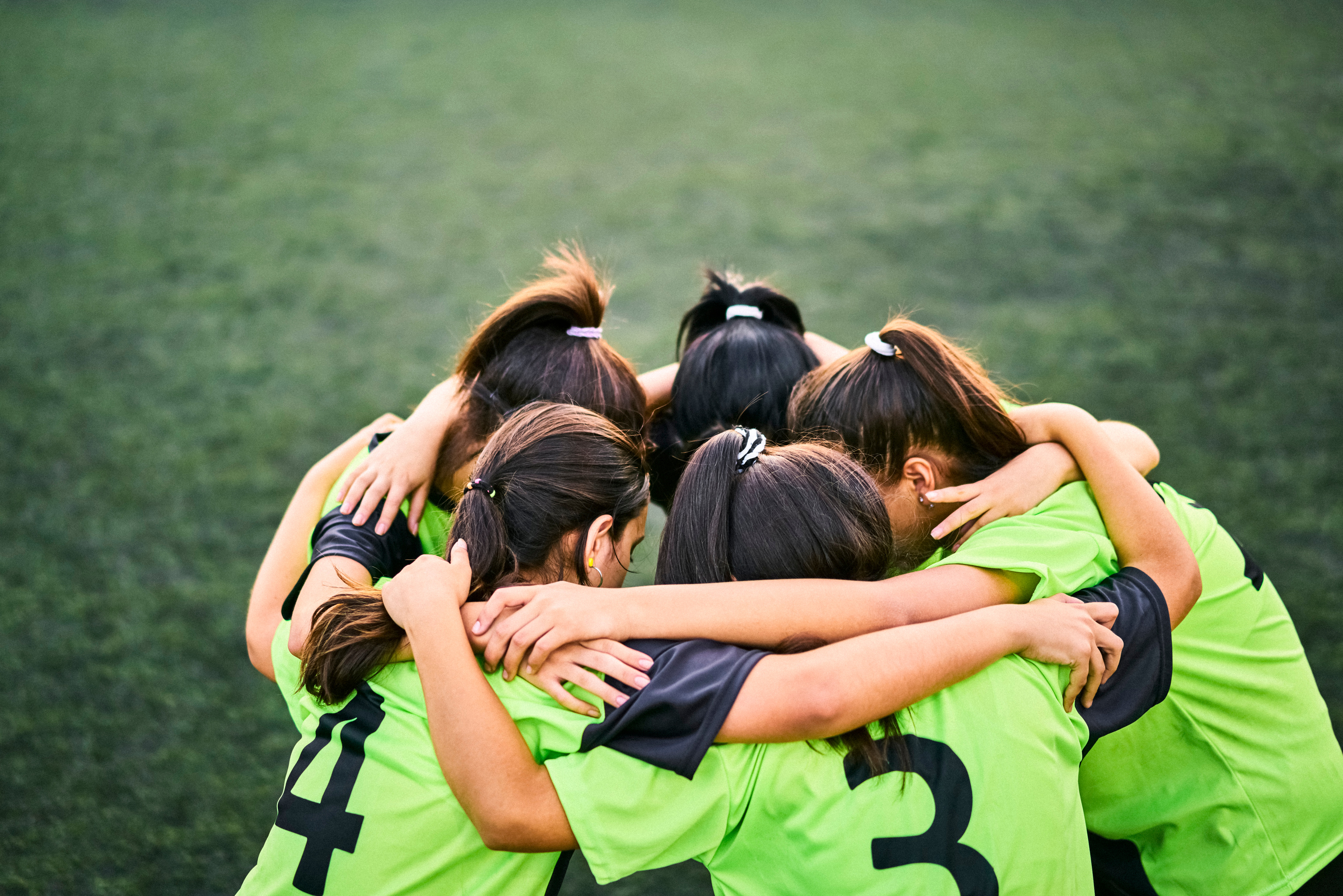 Girls soccer team discussing game plan in a huddle on field